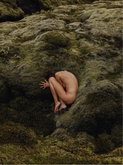 Artistic photo of a woman making herself small, sitting quietly in moss, representing vulnerability and seeking support in nature’s calm.