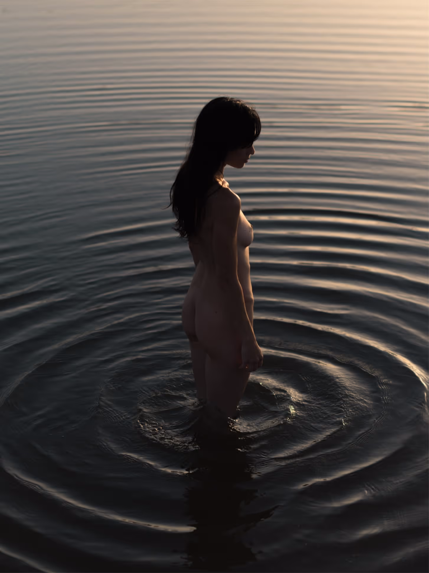 Woman standing knee-deep in calm water, creating ripples that spread outward, symbolizing the impact of listening and communication.
